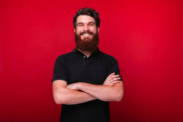 Bonito barbudo homem está sorrindo para a câmera com os braços cruzados . — Fotografia de Stock