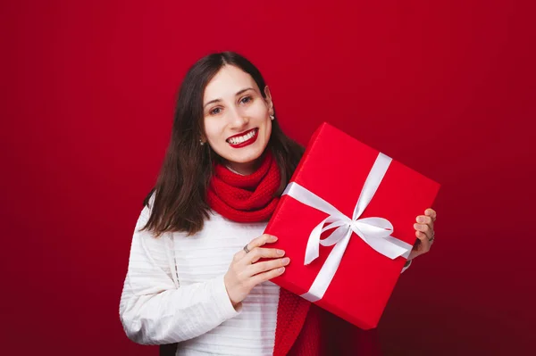 Schöne junge Frau hält großes rotes Geschenk über rotem Hintergrund — Stockfoto
