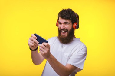 Sakallı adamın cep telefonuyla oynarken ve kulaklık kullanırken çekilmiş fotoğrafı