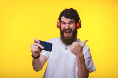 Yakışıklı sakallı adam mobil oynayan ve başparmak üzerinde gösteren