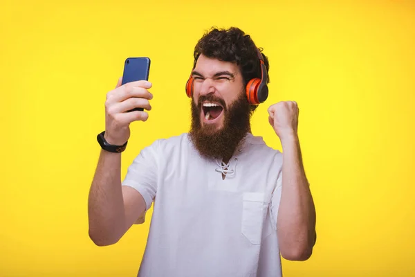 Homme barbu excité, avec casque, tenant un téléphone portable et — Photo