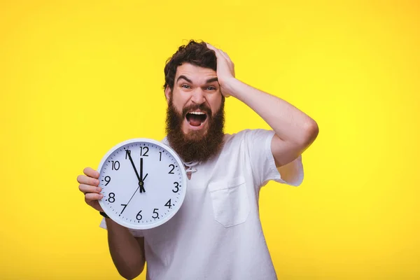 Un chico guapo molesto, sosteniendo un reloj sobre un fondo amarillo — Foto de Stock