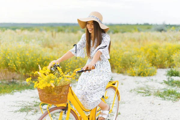 Foto de una mujer joven y bonita, en vestido y sombrero, en bicicleta en una f — Foto de Stock