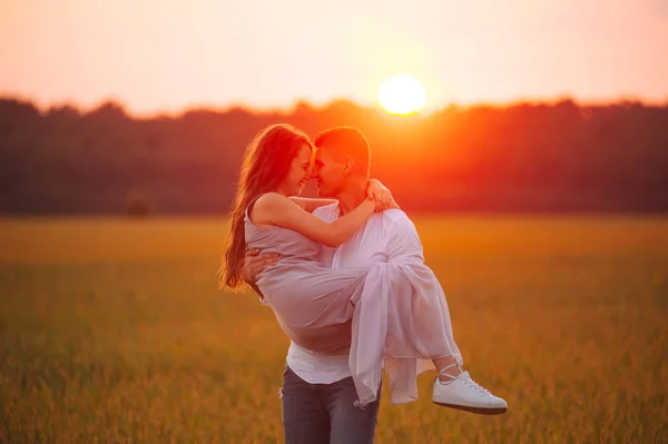 Foto de um casal, ele carregando ela em mãos no pôr do sol — Fotografia de Stock
