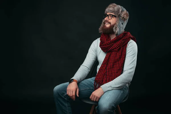 Perfil retrato de homem jovem em roupas de inverno olhando para longe enquanto sentado na cadeira em estúdio — Fotografia de Stock