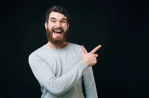 Fröhlicher Mann mit Bart in lässigem Wegzeigen vor dunklem Hintergrund — Stockfoto
