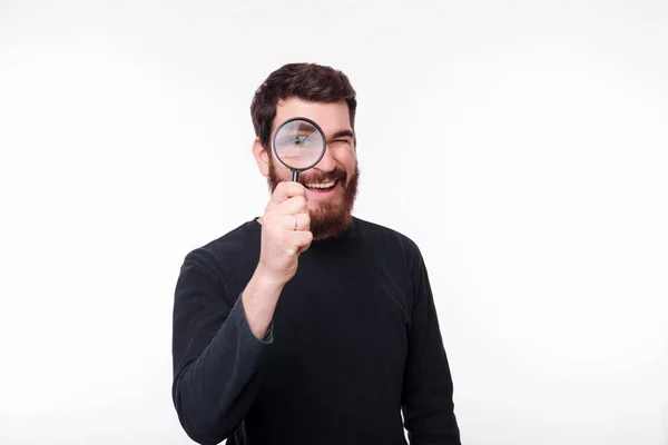 Handsome bearded man watching you through a magnifying glass on white background. — Stock Photo, Image