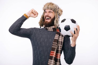 Sakallı adam, elinde futbol topu ya da futbol topu tutarken sakallı bir adamın yaptığı jesti kazandı. Kış giysileri. Futbol ya da futbol topu..