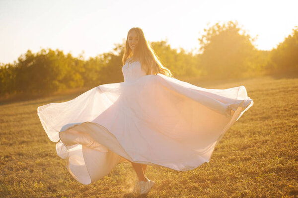 Happy blonde girl is whirling her dress on a field in the sunlight.