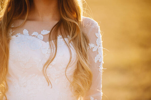 Close up photo of upper part a white wedding dress on a blonde girl in the sunlight