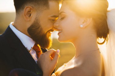 İki yeni evli çiftin, gün batımında yüz yüze duran ve gülümseyen sıcak bir portresi..