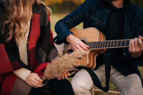 A young couple sitting and playing to the guitar on a field. — Stock Photo, Image