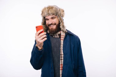 Kışlık giysiler içinde gülümseyen adamın fotoğrafı akıllı telefonuna bakıyor.