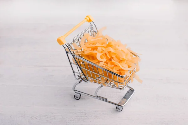 Foto de cerca de un pequeño carrito de compras con pasta sobre fondo de madera blanca —  Fotos de Stock