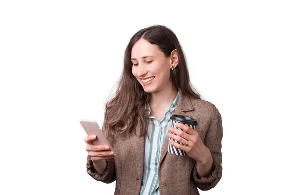 Retrato de alegre jovem mulher de escritório em terno olhando para smartphone e segurando xícara de café para ir — Fotografia de Stock