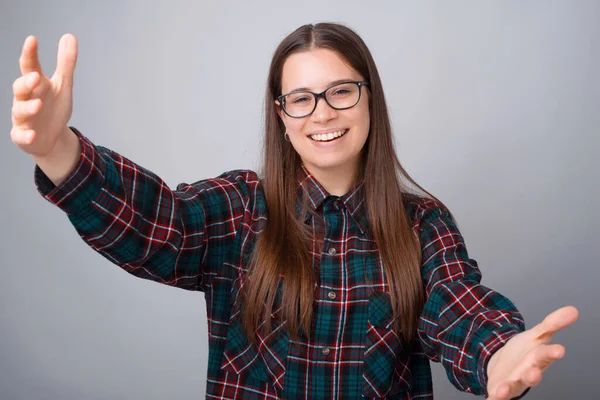 Retrato de una joven sonriente de pie sobre una pared blanca y haciendo un gesto de bienvenida — Foto de Stock