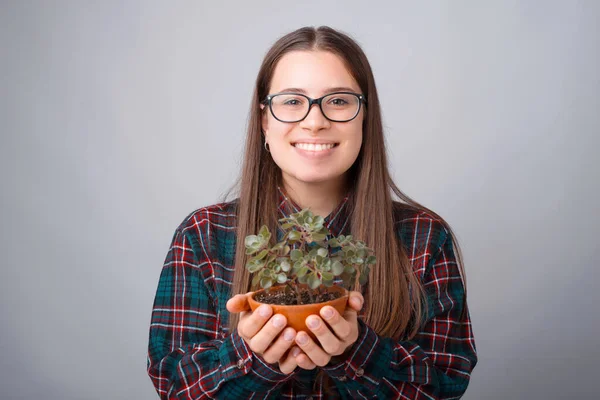 Foto de una linda mujer joven sosteniendo la planta de flores y mirando a la cámara — Foto de Stock