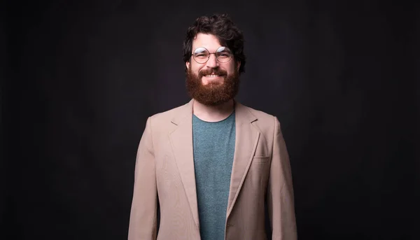 Foto de hombre barbudo sonriente en traje de pie sobre fondo negro —  Fotos de Stock