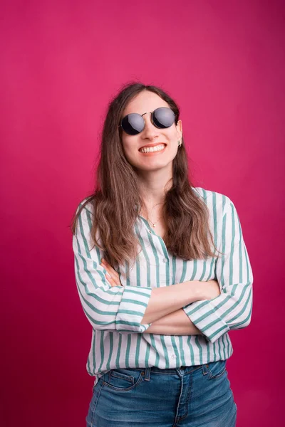 Χαμογελαστή κοπέλα με σταυρωμένα χέρια φοράει γυαλιά ηλίου πάνω από ροζ φόντο — Φωτογραφία Αρχείου