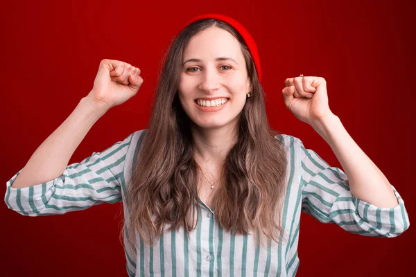 Sonriente chica está haciendo el gesto ganador sobre fondo rojo — Foto de Stock