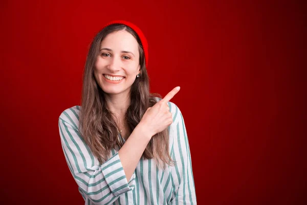 Schattige jonge vrouw wijst recht op rode achtergrond — Stockfoto