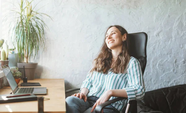 Söt ung kvinna tar en paus på sin arbetsplats medan hon sitter vid sitt skrivbord med växter — Stockfoto