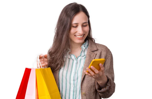 Молодая улыбающаяся женщина заказывает что-то на телефон, держа в руках сумки для покупок на белом фоне — стоковое фото
