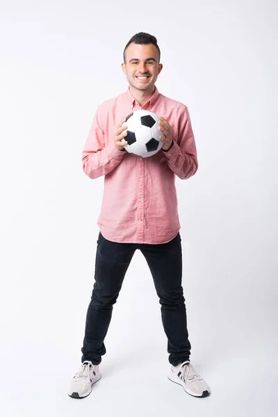 Heureux jeune homme sourit à la caméra tout en tenant un ballon de football sur fond blanc — Photo