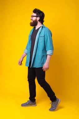 Neşeli sakallı adam sarı arka planda yürüyor. Tam vücut fotoğrafı..