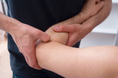 Erkek fizyoterapist bir adamın dirseğine bastırıyor ve derin masaj yapıyor..