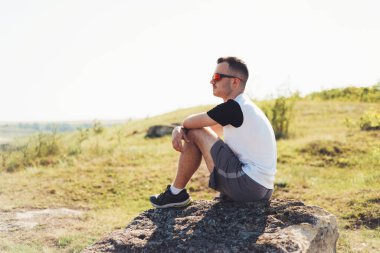 Düşünen bir adamın bir kayanın üzerinde oturup dinlendiğini ve uzaklara baktığını düşün.