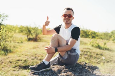 Gülümseyen genç bir adamın fotoğrafı ya da güneşli bir günde bir kayanın üzerinde otururken yaptığı jest gibi.