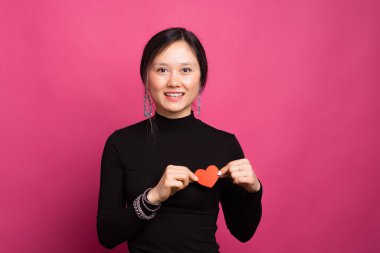 Mutlu gülümseyen kadın göğsünde kırmızı kağıt bir kalp taşırken kameraya bakıyor.