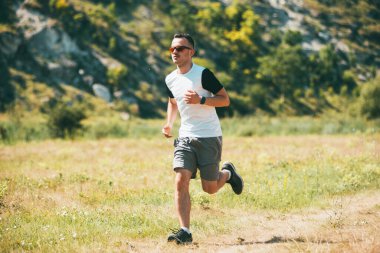 Genç adam güneş gözlüğü takıp açık havada koşuyor. 