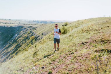 Genç adam güneşli bir günde koşuyor, yürüyor ya da bir tepede yürüyor..