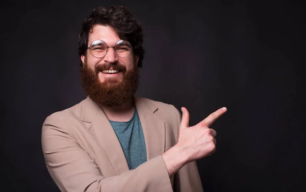 Foto av skäggig hipster man ler och pekar bort — Stockfoto