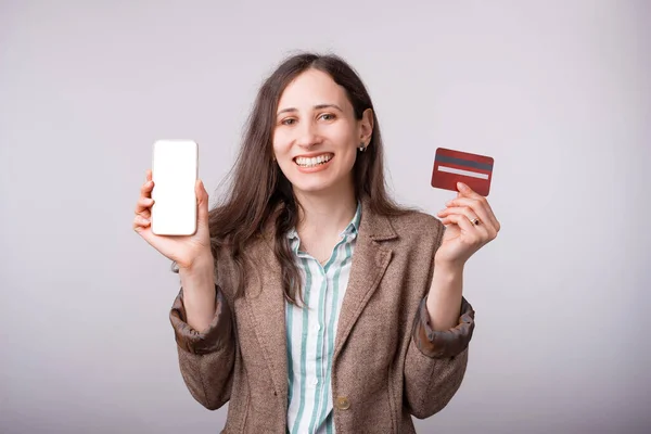 Sorrindo jovem mulher está segurando um telefone e cartão sobre fundo branco — Fotografia de Stock