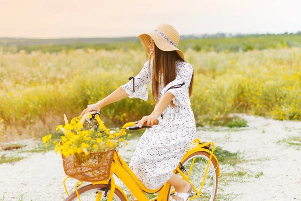 Mujer joven sonriente está montando su bicicleta amarilla en un campo — Foto de Stock