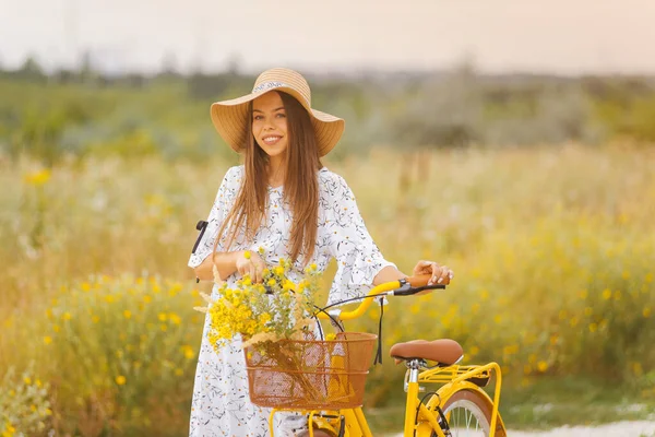 Uśmiechnięta młoda dama spaceruje z rowerem po polu żółtych kwiatów — Zdjęcie stockowe