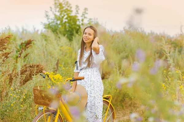 Wspaniała młoda kobieta stoi tuż obok swojego żółtego roweru na polu — Zdjęcie stockowe