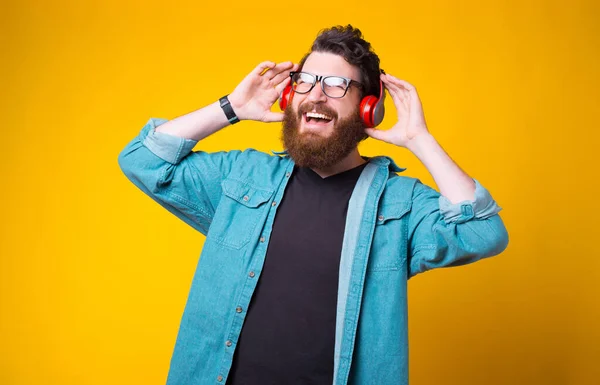 Alegre barbudo hipster está escuchando la música a través de auriculares sobre fondo amarillo —  Fotos de Stock