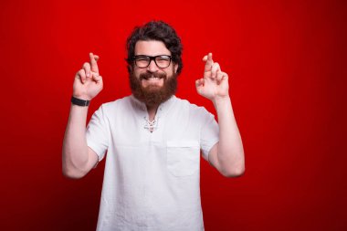 Neşeli sakallı adam kırmızı arka planda umut veya dilek jesti yapıyor..