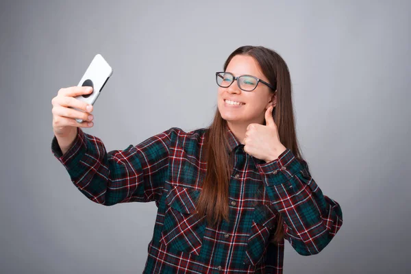 Jovencita está haciendo una selfie con su teléfono sobre fondo gris — Foto de Stock
