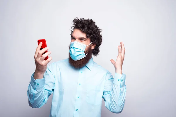 Foto av ung man ser förvånad på smartphone när du bär medicinsk mask — Stockfoto