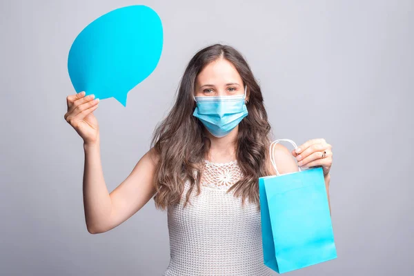 Retrato de mulher jovem usando máscara medicinal e segurando bolha de fala vazia e saco de compras — Fotografia de Stock