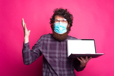 Maske takan ve boş laptop ekranı gösteren kafası karışık bir adam portresi