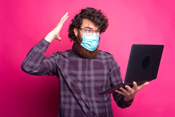 Tıbbî maske takan ve dizüstü bilgisayara bakan genç adamın fotoğrafı. — Stok fotoğraf