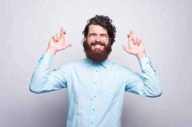 Mavi tişörtlü sakallı hippi adam beyaz duvarın üzerinde şans diliyor..