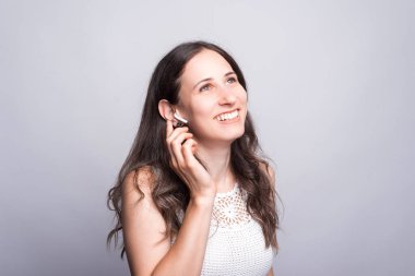 Gülümseyen ve beyaz duvarın üzerinde kulaklık kullanan neşeli genç bir kadın..