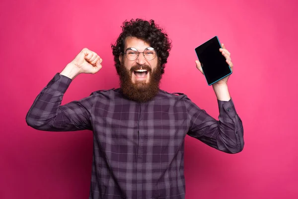 Foto do jovem com as mãos levantadas comemorando o sucesso e hiolding tablet — Fotografia de Stock